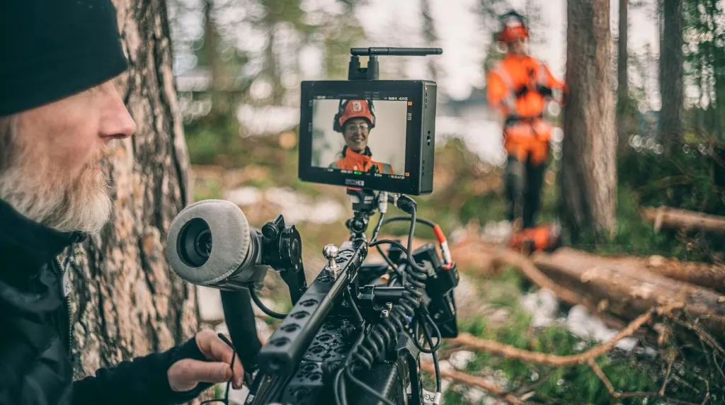Filmfotograf filmar Olivia i skyddsutrustning i skogen, hon syns på kamerans skärm